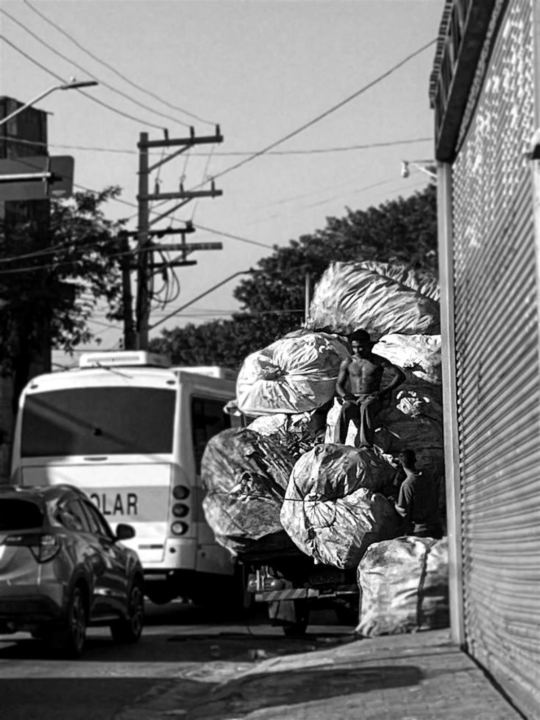 Caminhão carregado com sacos enormes de recicláveis parado no meio da rua.