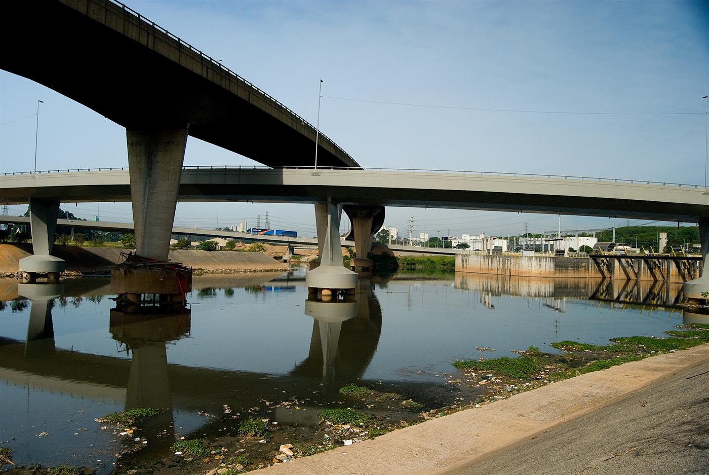 Rio Tietê poluído passando embaixo de um viaduto.